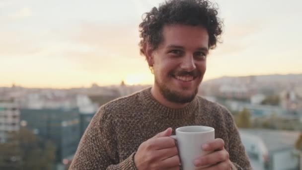 笑着站在阳台上用杯子喝咖啡的年轻人 — 图库视频影像