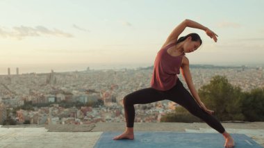 Genç bir kadın gün doğumunda izleme platformunda yoga yapıyor.