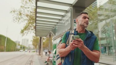 Tramvay durağında dururken elinde cep telefonu olan orta yaşlı bir adam.