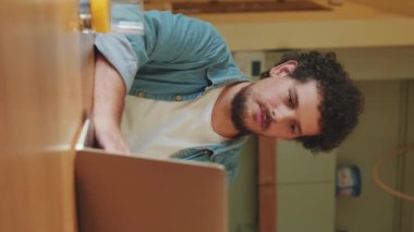 Genç bir erkek dizüstü bilgisayar kullanıyor, mutfakta serbest çalışıyor.