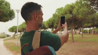 Şehir parkında dikilirken fotoğraf çeken orta yaşlı turist.
