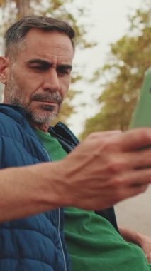 Orta yaşlı erkek turist park bankında otururken cep telefonu kullanıyor