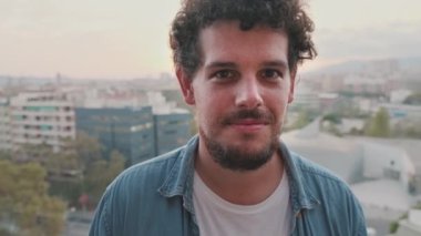 Balkonda dikilirken kameraya poz veren gülümseyen genç adamın yakın çekimi.