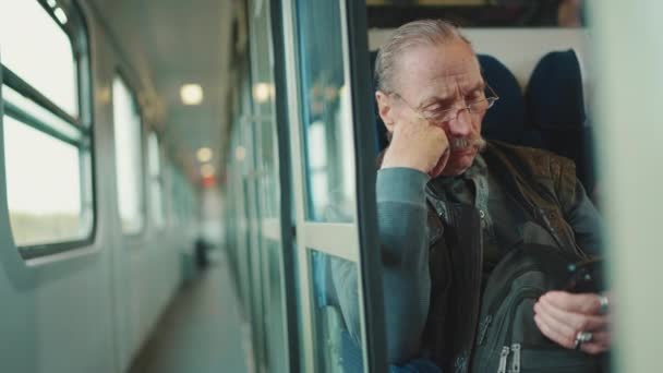 坐火车旅行时 戴眼镜的多愁善感的老年人使用手机 — 图库视频影像