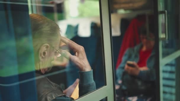 坐火车旅行时 戴眼镜的老年人用手机 透过玻璃看 — 图库视频影像