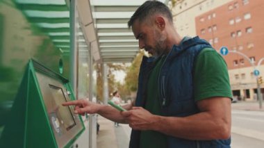 Orta yaşlı bir adam akıllı telefon kullanarak toplu taşıma biletini ödüyor.