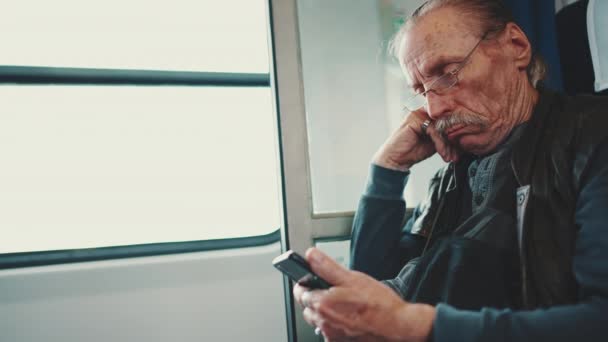 坐火车旅行时 戴眼镜的老年人使用手机 — 图库视频影像
