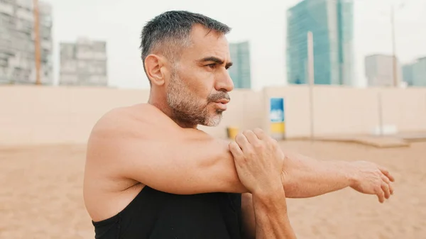 成熟的运动员站在海滩上伸展手臂肌肉 — 图库照片