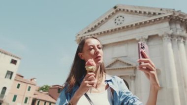 Uzun kahverengi saçlı, mavi gömlekli güzel bir kız. Dondurmadan hoşlanıyor ve eski kasaba meydanında beklerken cep telefonuyla selfie çekiyor.