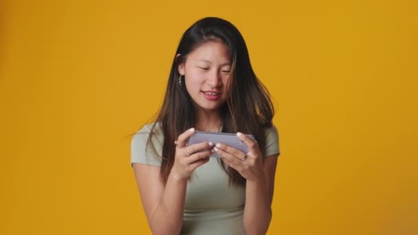 Усміхнена Молода Жінка Грає Мобільному Телефоні Ізольовано Жовтому Фоні Студії — стокове відео