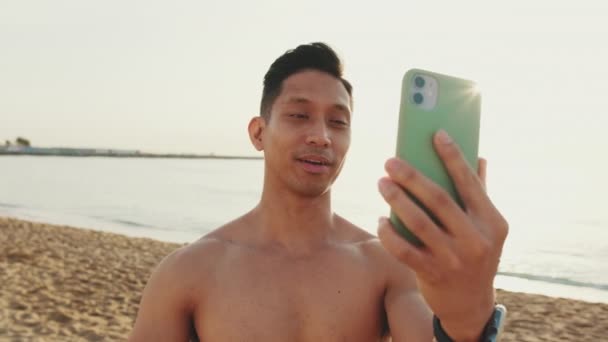 Молодой Спортсмен Стоящий Пляже Делает Видеозвонок Мобильного Телефона — стоковое видео