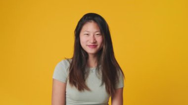 Stüdyoda sarı arka planda, kameraya bakan ve gülen genç bir kadın.