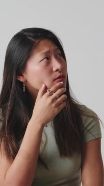 Düşünen ve karar veren genç bir kadın stüdyoda beyaz bir arkaplan üzerinden izole edilmiş.