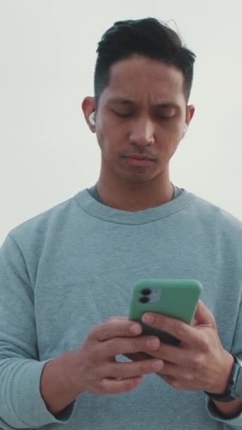 ワイヤレスヘッドフォンの若者が橋の上に立って携帯電話を使う — ストック動画