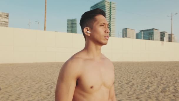 若い運動選手がヘッドフォンでビーチに立っている — ストック動画