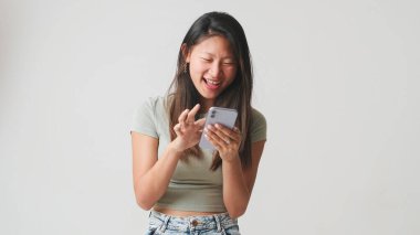 Akıllı telefon ekranında gri tomarlı mutlu kız, sosyal ağlara göz atıyor, iyi haberler alıyor, beyaz arka planda izole edilmiş iyi mobil uygulamalar kullanıyor, stüdyo çekimi.