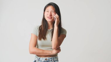 Gri bluzlu gülümseyen kız cep telefonuyla konuşuyor. Beyaz arka planda izole edilmiş, stüdyo çekimi.