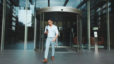 Genç işadamı akıllı telefonuyla iş merkezinden ayrılıyor.