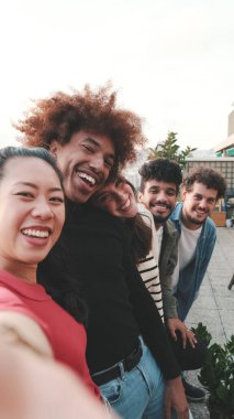 Balkonda durup cep telefonuyla selfie çeken gençlerin yakın çekimi.