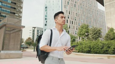 Elinde cep telefonu olan genç bir işadamı iş merkezinin önünden geçiyor.