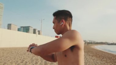 Sahilde duran genç atletik adam kaslarını ısıtıyor.