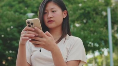 Şehir parkında bankta oturan genç bir kadın, cep telefonu kullanıyor.