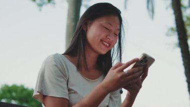 Dışarıda bankta otururken cep telefonu kullanan genç bir kadın.