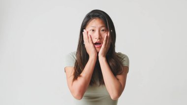 Gri bluzlu kız şaşkınlıkla el kaldırıyor kameraya bakıyor, sevinçten uçuyor beyaz arka planda izole edilmiş iyi haberlerle, stüdyo çekimleriyle