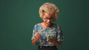 Gözlüklü, mavi tişörtlü bir kız cep telefonundan harika haberler okuyor, zaferi yeşil-mavi arka planda kutluyor.