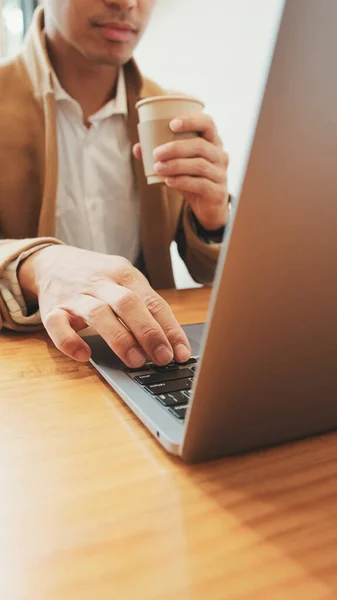 stock image Young businessman wearing beige suite sits at table with laptop and drinks coffee