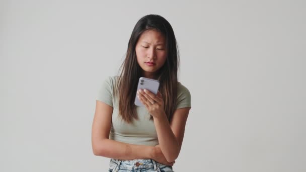 年轻的女人看着手机在演播室里选择一些独立于白色背景的东西 — 图库视频影像
