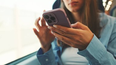 Mavi gömlekli, uzun kahverengi saçlı tatlı kız, tren yolculuğu sırasında akıllı telefon ekranına kayıyor.