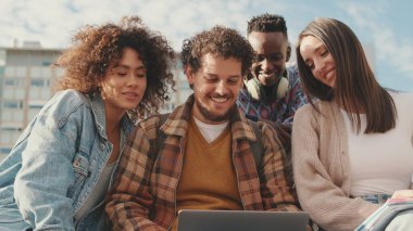 Dışarıda dizüstü bilgisayardaki bir şeye gülen mutlu arkadaşlar. Dört öğrenci birlikte vakit geçiriyor.