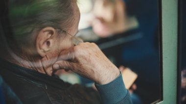 Yakın plan, düşünceli yaşlı adam tren coupe ile seyahat ederken cep telefonu kullanıyor, camdan bakıyor.