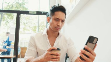 Genç işadamı cep telefonuyla masada oturuyor ve kafede kahve içiyor.