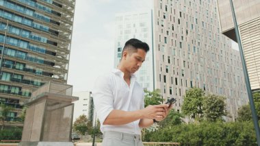 Genç işadamı iş bölgesinde dururken akıllı telefonuyla yazı yazıyor.