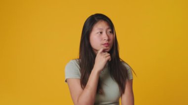 Düşünen ve karar veren genç bir kadın sarı arka plandan izole edilmiş stüdyoda.