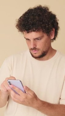 Stüdyoda elinde bej arka planda cep telefonu olan şaşırmış bir adam.