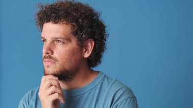 Yakından, dalgın adam bir şey düşünüyor, stüdyoda mavi arka planda izole edilmiş.