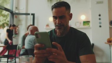 Kafede oturan orta yaşlı bir adam cep telefonu kullanıyor.