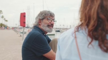 Mutlu yaşlı adam marinada iskelede oturuyor ve kız arkadaşını dikkatle dinliyor.