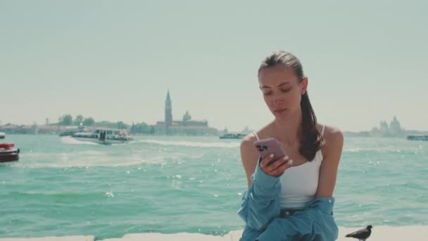Piękna Dziewczyna Długimi Brązowymi Włosami Ubrana Niebieską Koszulę Siedzi Nabrzeżu — Wideo stockowe