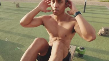 Genç adam dışarıda spor alanında karın kaslarını çalıştırıyor.