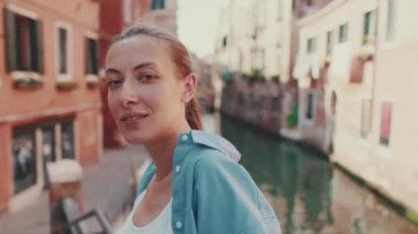 Uzun kahverengi saçlı, mavi gömlekli güzel bir kızın yakın çekimi. Venedik 'te, eski şehirde ve arka planda kameraya poz veriyor.