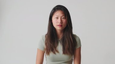 Genç bir kadın kameraya bakarken şaşkınlıkla el kaldırıyor. Stüdyoda beyaz arka planda izole edilmiş.