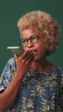 Genç bir kadın mavi arka planda izole edilmiş bir cep telefonundan sesli mesaj gönderiyor.