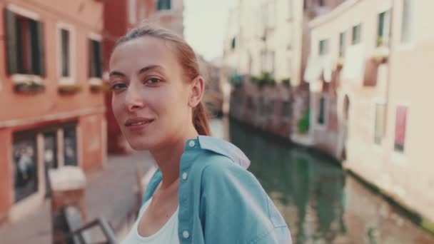 在威尼斯 古城和运河的背景上 身着蓝色衬衫 一头棕色长发的美女在镜头前摆姿势拍照 — 图库视频影像