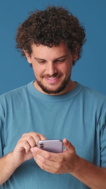 Усміхнений Чоловік Тримає Телефон Студії Синьому Фоні — стокове відео