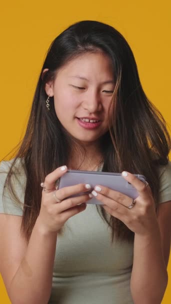 Lachende Jonge Vrouw Spelen Mobiele Telefoon Geïsoleerd Gele Achtergrond Studio — Stockvideo