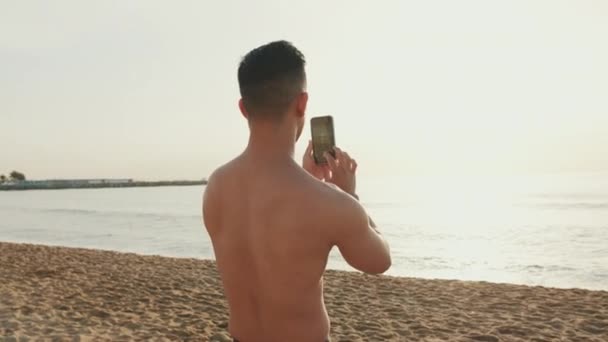 Joven Atlético Parado Playa Filmando Video Teléfono Móvil — Vídeos de Stock